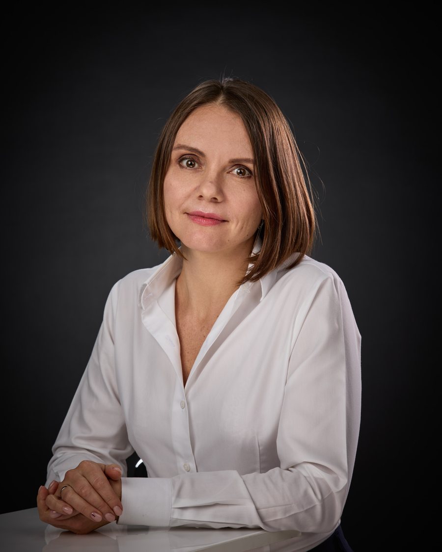Agnieszka Baran w białej koszuli, przy stole, z dłońmi splecionymi przed sobą